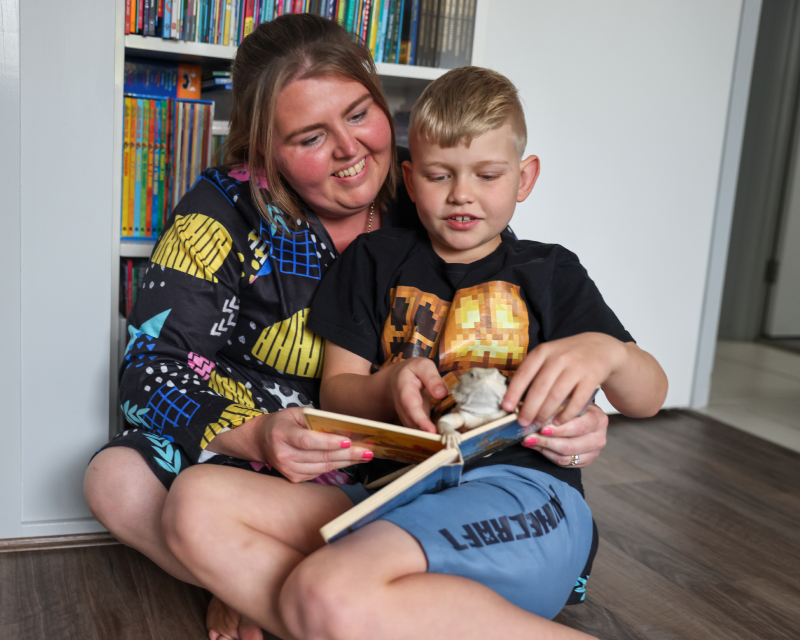 Young boy sitting on the lap of a woman, reading a book together.